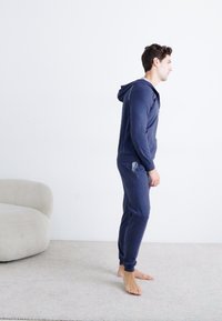 Námořnickomodrý hoodie a jogger set vyrobený z měkké tkaniny, s úzkým střihem, předními kapsami a texturovaným povrchem.