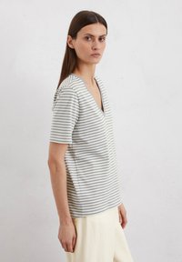 Striped v-neck t-shirt in light gray and white, short sleeves, relaxed fit, soft texture, with a subtle neckline trim detail.