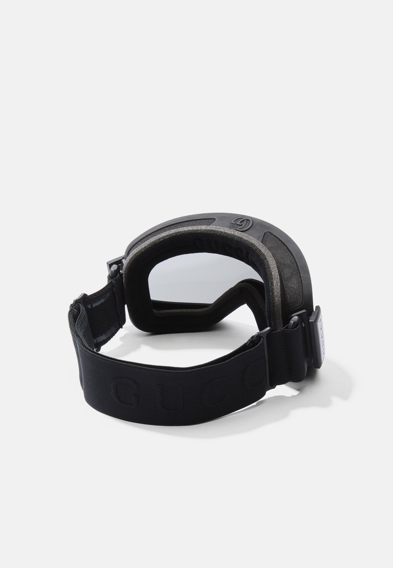 Black ski goggles with a padded frame, clear lenses, and an adjustable elastic strap featuring embossed branding on the band.