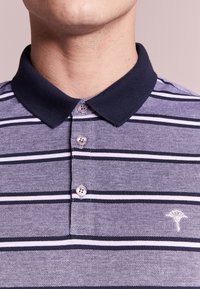 Polo en coton avec col marine, motif rayé blanc et marine, patte de boutonnage à trois boutons, tissu texturé et petit logo brodé sur la poitrine.