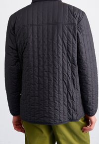 Pikowana czarna kurtka z długimi rękawami, z poziomym przeszyciem, zaokrąglonym dołem i wysokim kołnierzem. Materiał wydaje się lekki i teksturowany.