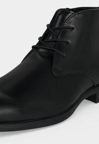 Botte habillée en cuir noir avec lacets, bout arrondi et talon bas sur un fond clair uni.