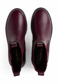 Par de botas Chelsea de cuero rojo oscuro con suelas negras y tiradores, vistas desde arriba sobre un fondo blanco.