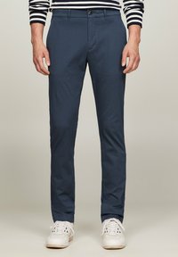 Pantaloni slim-fit blu scuro realizzati in tessuto leggero con una trama liscia. Presentano una chiusura con bottone e tasche frontali.