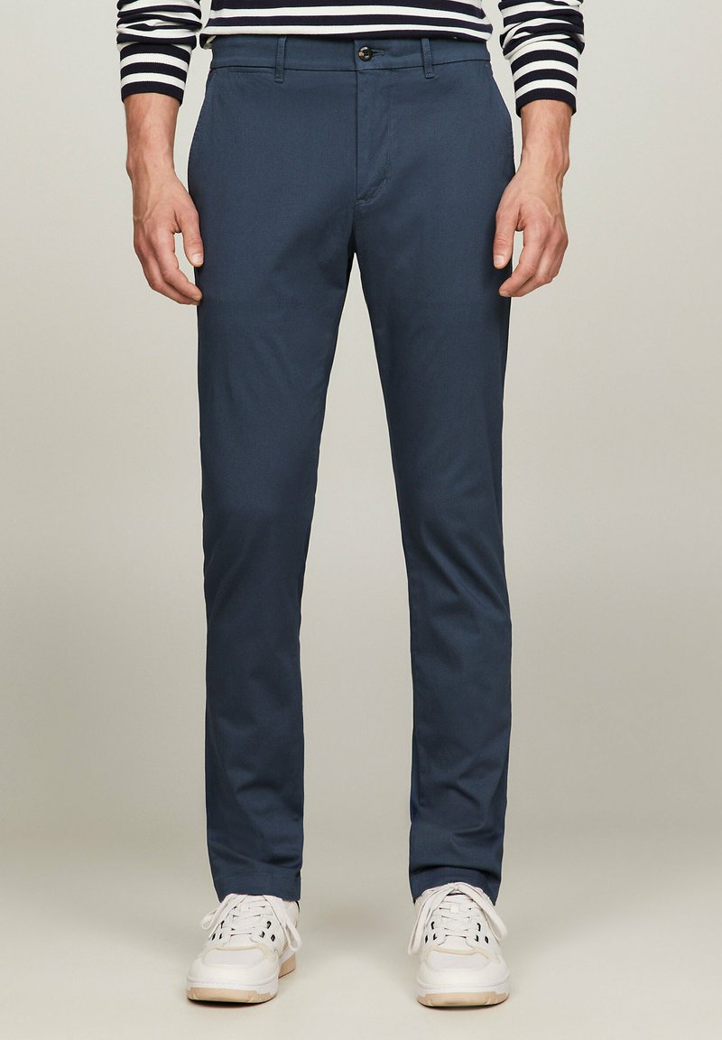 Pantaloni slim-fit blu scuro realizzati in tessuto leggero con una trama liscia. Presentano una chiusura con bottone e tasche frontali.