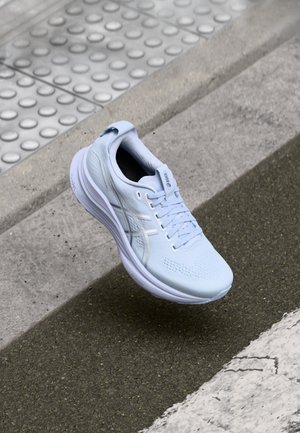 Zapatilla de correr azul claro con una parte superior texturizada, suela blanca y un logotipo sutil. Presenta cordones y una tira en el talón para facilitar su uso.