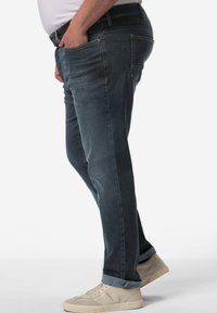 Jeans de mezclilla oscuros con corte recto, que cuentan con bolsillos delanteros y un leve desgastado. Combinados con zapatillas de color claro.