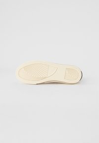 Witte rubberen sneakersole met een ingewikkeld tractiepatroon. Geprofileerd logo detail nabij de hiel. Vlotte randen en een afgeronde te ontwerp.