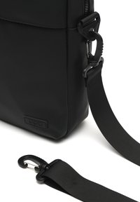Borsa a tracolla nera realizzata in materiale sintetico morbido, con chiusura a zip, tracolla staccabile e clip metallica per un attacco sicuro.