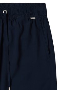 Marineblå elastiske shorts med snøre i taljen og sidelommer med et lille sølvfarvet mærke tæt på lommen.