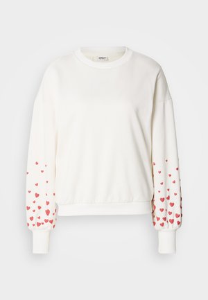 Hvit genser med lange ermer og et mønster av små røde hjerter langs mansjettene. Mykt stoff med ribbet hals og kant.