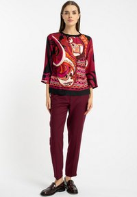 Czarna i czerwona bluzka w wzory z rękawami do trzech ćwiartek, zestawiona z buraczkowymi spodniami typu tapered i ciemnymi loafersami. Gładka faktura, żywy design.
