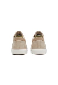 Zapatillas de ante beige con acentos texturizados, suela de goma blanca y talón trasero en contraste. Diseño minimalista con forma redondeada y estilo sin cordones.