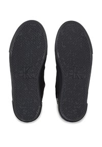 Suelas de zapatillas de goma negra con patrón de agarre texturizado y logo en relieve "Calvin Klein Jeans" cerca del talón. Diseño plano y ancho.