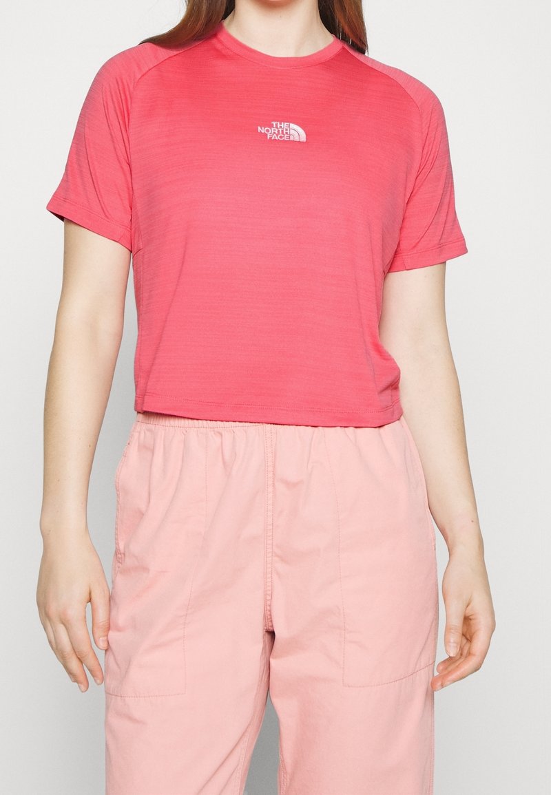 Krátké tričko s krátkým rukávem v jasně růžové barvě s jemnou horizontální texturou. Na hrudi je bílá logo. Kombinováno s lehkými růžovými kalhotami.