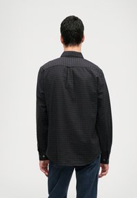 Fekete gombos ing, lila és zöld kockás mintával, hosszú ujjal és klasszikus gallérral; ívelt alj és gombos mandzsetta.