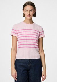 Rebrasti kratki top u svijetlo ružičastoj boji s horizontalnim ružičastim prugama. Ima okrugli izrez i teksturiranu tkaninu. Uparen s tamnim trapericama.