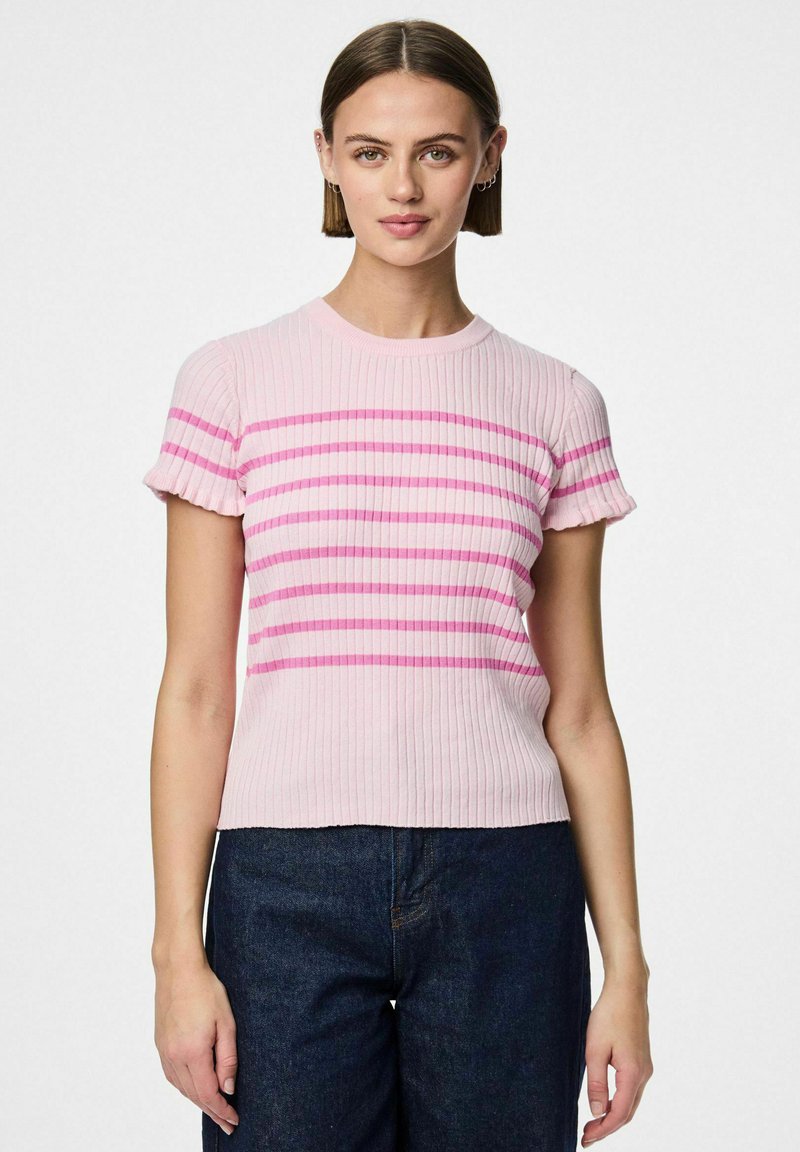 Rebrasti kratki top u svijetlo ružičastoj boji s horizontalnim ružičastim prugama. Ima okrugli izrez i teksturiranu tkaninu. Uparen s tamnim trapericama.