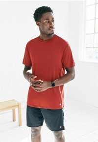 Herren Sport-T-Shirt mit kurzen Ärmeln in leuchtendem Rot, aus glattem Stoff mit Rundhalsausschnitt; kombiniert mit schwarzen Shorts, schlichtes Design, ohne Muster.