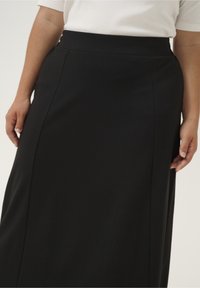 Zwarte, lange rok met een gladde textuur, hoge tailleband en zijsplit-details. Gemaakt van een rekbare stof voor comfort.