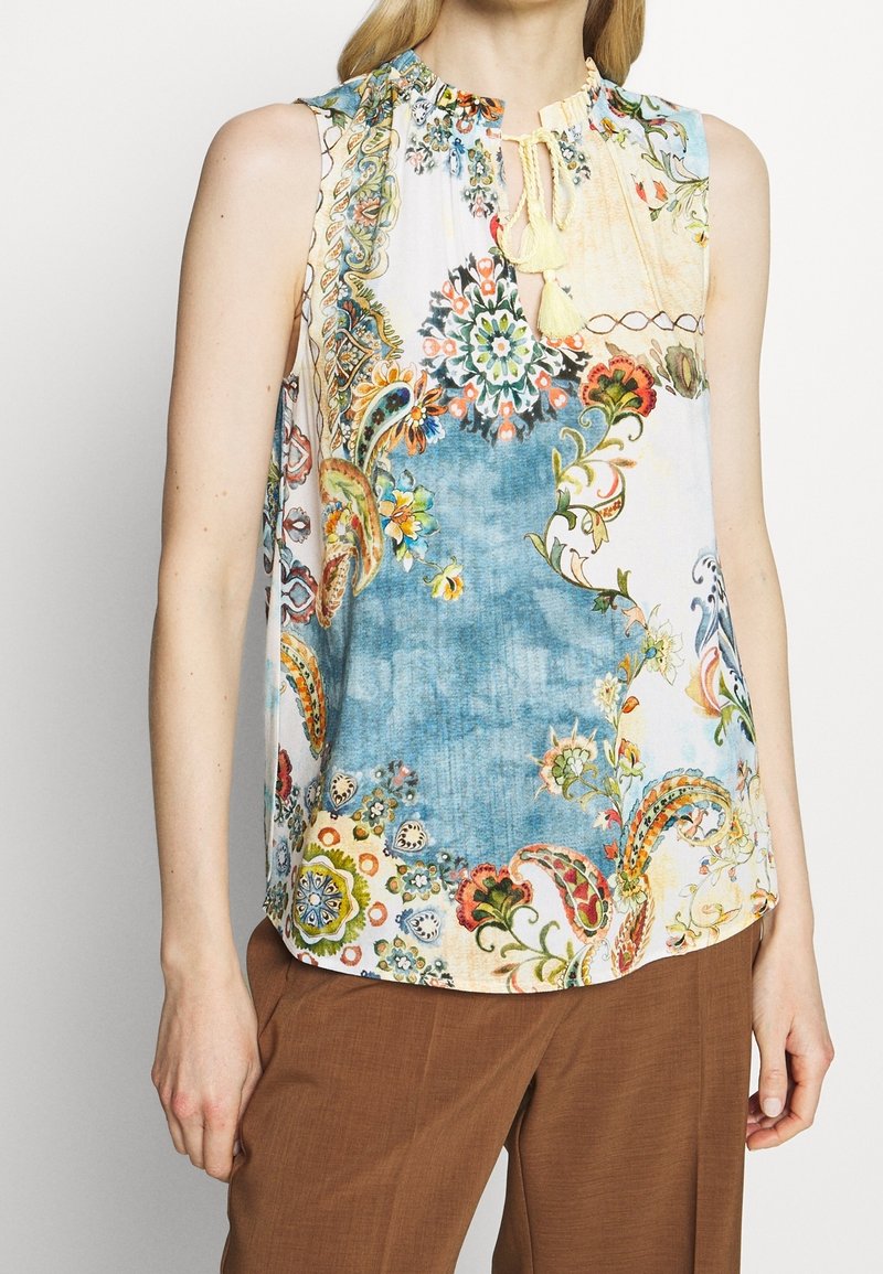 Blouse sans manches avec un motif floral et paisley vibrant dans des teintes de bleu, d'orange et de vert, avec un décolleté rond et un tissu texturé.