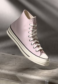 Høye sneakers i lys rosa lerret med hvite lisser, gummitopp, og to-tonet teksturert såle med en svart stripe langs kanten.