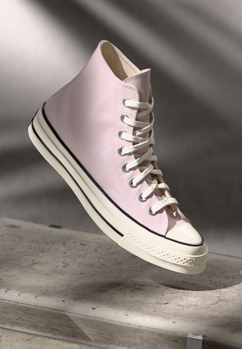 Høye sneakers i lys rosa lerret med hvite lisser, gummitopp, og to-tonet teksturert såle med en svart stripe langs kanten.
