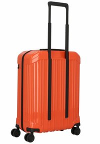 Hard shell orange suitcase with vertical ridges, black telescopic handle, and four wheels for mobility. Durable plastic material.
