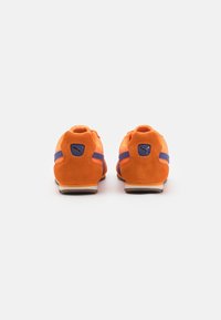 Pomarańczowe zamszowe sneakersy z fioletowymi akcentami, zaokrąglonym kształtem, gumową podeszwą i małym logo na pięcie.