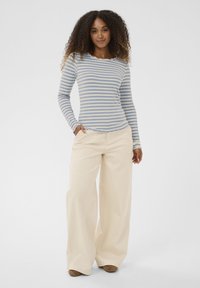 Langærmet top med ribstruktur og blå-hvide vandrette striber; krave med bølget kant. Kombineret med beige bukser med vide ben og brune sko.