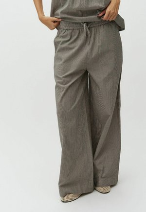 Személy laza, szürke cseppsávos, bő szárú nadrágot visel elasztikus derékrésszel és húzózsinórral, bézs színű, szőtt, bebújós cipővel párosítva.