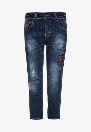 Jean en denim bleu foncé à coupe slim, avec des empiècements usés, des surpiqûres contrastantes et diverses textures de tissu.