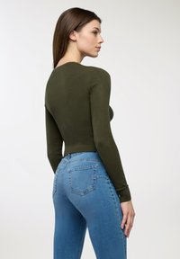 Oliwkowa bluzka z długim rękawem o dopasowanym kroju, zestawiona z jasnoniebieskimi dżinsami z wysokim stanem, posiadającymi tylne kieszenie i subtelną fakturę.