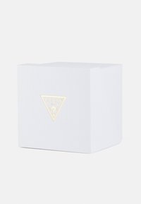Weißer, strukturierter Karton mit einem goldenen, dreieckigen Guess-Logo auf der Vorderseite, das ein sauberes, kantiges Design und eine subtile, minimalistische Ästhetik aufweist.