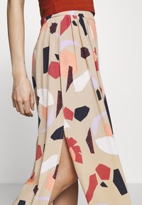 Beige hame, jossa on korkea halkio, ja rohkeita abstrakteja muotoja punaisena, tummansinisenä, vaaleanpunaisena ja valkoisena. Kevyt kangas kerätyllä vyötäröllä.