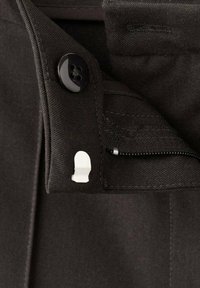 Cinturilla de tela negra con un botón y una cremallera blanca. Detalles en primer plano muestran la textura cosida y un lazo adicional de tela.