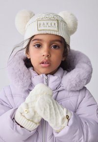 Fehér sapka bojttal és arany hímzéssel, krémszínű, texturált mintás és szív alakú díszítéssel rendelkező kesztyűkkel, levendula színű kabát mellé párosítva.