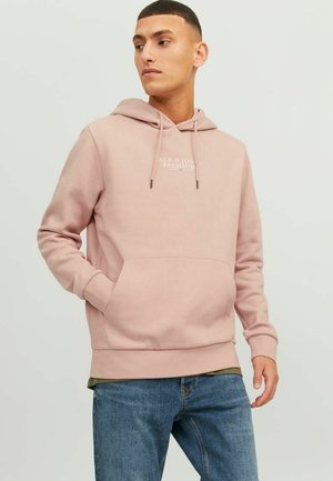 Pink hoodie with drawstrings, kangaroo pocket, and front logo. Soft fabric, relaxed fit, ribbed cuffs, and hem; paired with blue jeans.