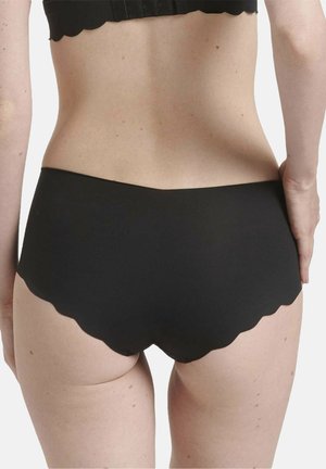 Donna che indossa biancheria nera con bordo smerlato e reggiseno abbinato, mostrata di spalle con una mano appoggiata sul fianco.