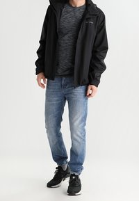 Black waterproof jacket over a gray striped T-shirt, paired with light blue jeans and black sneakers with gray accents.