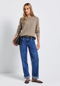 Beige strikket sweater, blå afslappede jeans med opbrettede bukseben, og sort geometrisk clutch. Modellen bærer flade sorte mesh-sandaler.