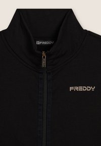 Giacca nera con zip realizzata in tessuto morbido, dotata di colletto alto, dettagli della zip tono su tono e logo impresso sul petto.