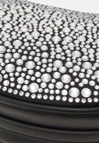Bolso circular de piel negra adornado con strass transparentes de diferentes tamaños, con una textura suave y numerosos detalles decorativos.