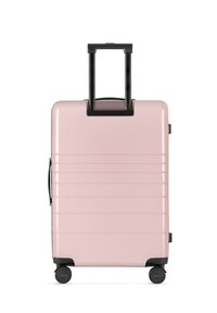 Valigia rigida di colore rosa chiaro, con scanalature orizzontali, un manico estensibile nero e quattro ruote nere per la mobilità.