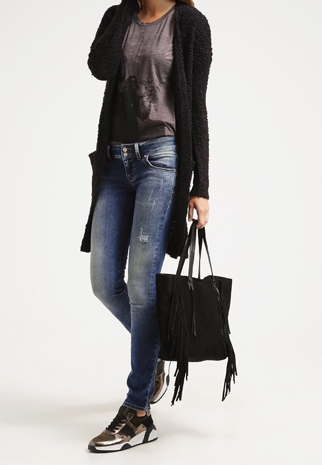 Black textured cardigan, gray graphic t-shirt, distressed blue jeans, black fringe tote bag, and silver sneakers with black accents.