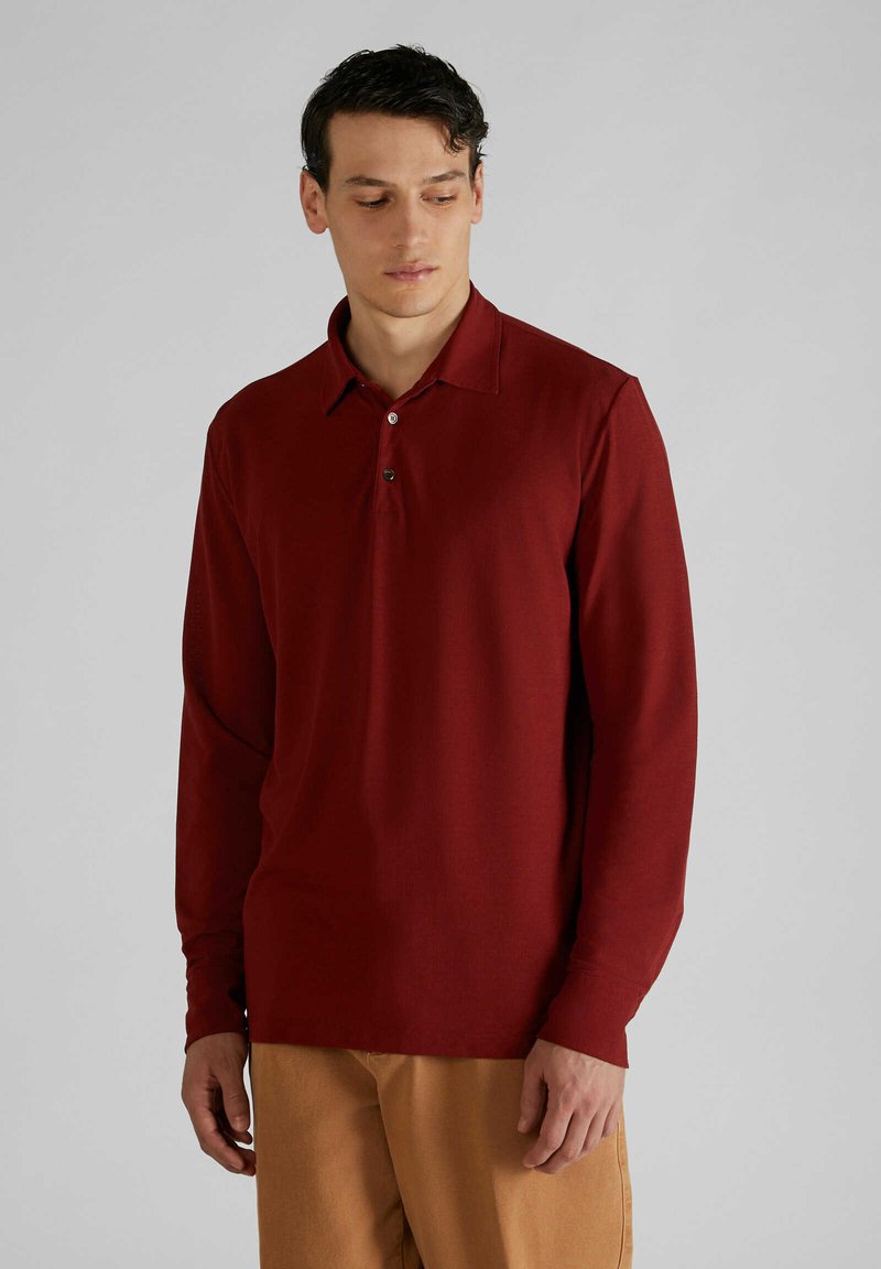 Polo a maniche lunghe di un profondo colore rosso. Presenta un colletto classico, una pattina con due bottoni e un tessuto liscio e texture.