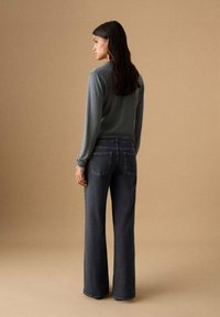 Pulover gri asortat cu blugi evazați cu talie înaltă din denim închis la culoare. Țesătură netedă cu un design curat; detalii minime de cusături, fără modele.