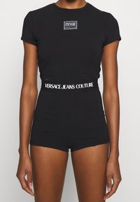 Svart figursydd t-shirt med korta ärmar och ett logotypmärke på bröstet, matchad med högmidjade svarta shorts med ett märkt midjeband.