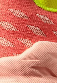 Idrettssko øverst i korall med et teksturert mønster og lys rosa overlegg, med pustende mesh-detaljer og lysegrønne accenter.