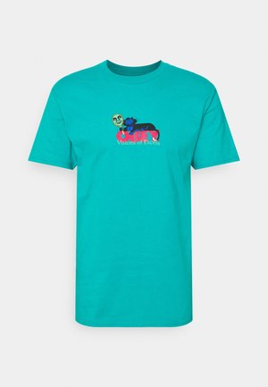 Turquoise T-shirt met een afbeelding van een zwarte kat die een rond gezichtsmasker boven rode tekst met de woorden "OBEY" en kleinere tekst "Visions of Excess" vasthoudt.